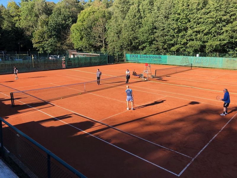 Tennisspieler auf klassischem ziegelroten Sandplatz mit weißen Markierungslinien.