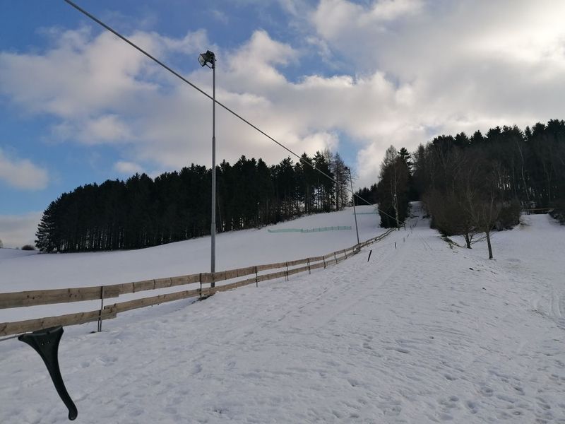 Verschneiter Skihang in Zwönitz mit Schlepplift-Anlage, Holzzaun und Waldrand