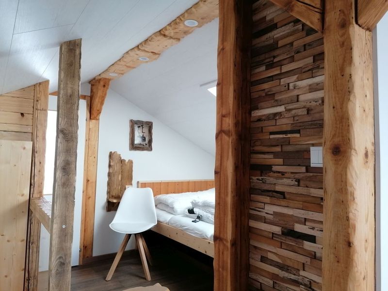 Übernachtungsbungalow mit Schlafboden - Rustikales Schlafzimmer mit Holzbalken, weißem Stuhl und Bett