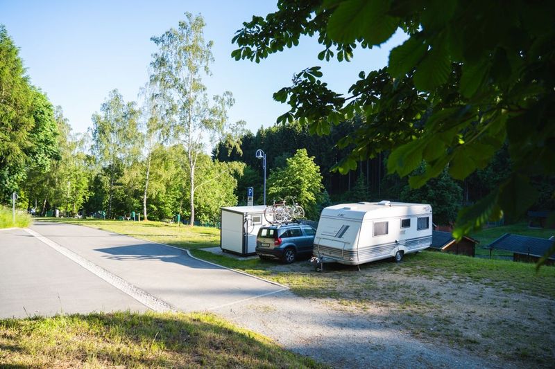 Idyllischer Campingplatz im Grünen mit einem Wohnwagen-Gespann, Fahrrädern und einer weiten Waldkulisse.  (Link öffnet das Foto vergrößert in einem Popupfenster)