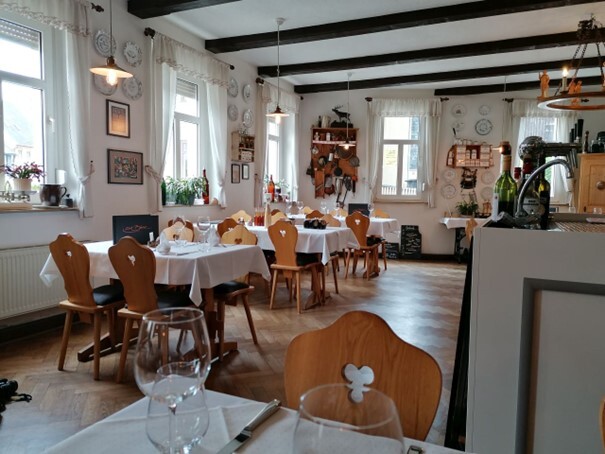 moderner Chic trifft gemütlich rustikales Flair Gemütlicher Gastraum mit weiß gedeckten Tischen, Holzstühlen und dekorativen Wandtellern. (Link öffnet Bild vergrößert in einem Popupfenster)