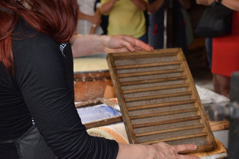 Handwerkerin mit rötlichem Haar hält einen hölzernen Schöpfsiebrahmen über einem Bottich zur Papierherstellung (Link öffnet Bild vergrößert in einem Popupfenster)