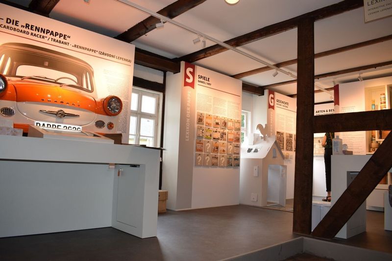 Ausstellungsbereich mit Informationstafeln zum Thema Pappe, einem Modellauto (Trabant) und hölzernen Deckenbalken. (Link öffnet Bild vergrößert in einem Popupfenster).