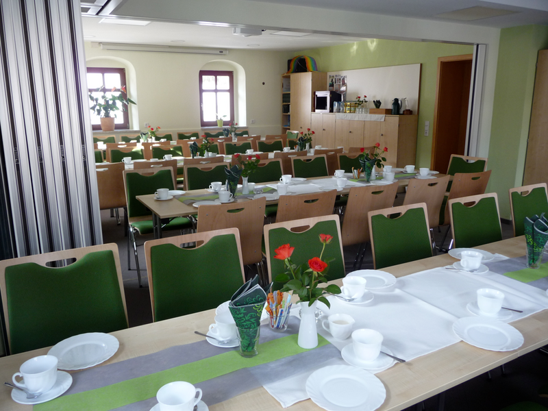 Großer Speisesaal mit festlich gedeckten Tischen, grünen Stühlen, weißen Tassen und roten Rosen in Vasen. (Link öffnet Bild vergrößert in einem Popup-Fenster)