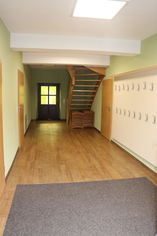 Heller Eingangsbereich mit Holzparkett, grünen Wänden, Garderobe, offener Treppe und dunkler Haustür. (Link öffnet Popupfenster mit vergrößertem Bild)