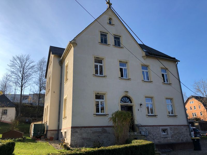 mehrstöckiges Pfarrhaus mit sandgelben Putz vor blauem Himmel (Link öffnet Bild vergrößert in einem Popupfenster)