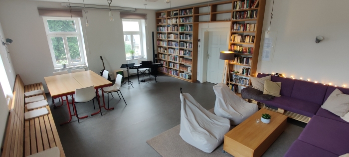 Gemütlicher Wohnraum mit lila Palettensofa, Sitzsäcken, großem Bücherregal, E-Piano und Esstisch. (Link des Bildes führt zu PopupFenster mit größerem Bild)