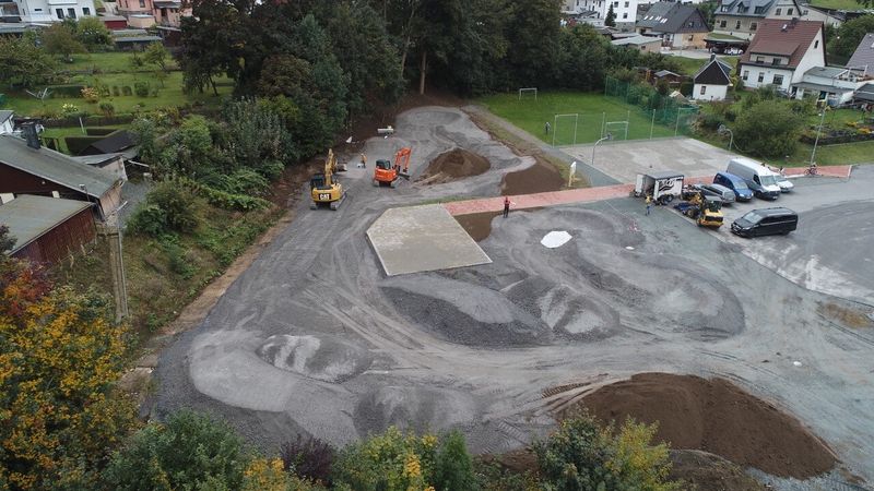 Vogelperspektive auf die Baustelle vom Pumptrack für einen Parcours mit Baggern, Erdhügeln und angrenzendem Sportplatz. (Link öffnet Bild vergrößert in einem Popupfenster).