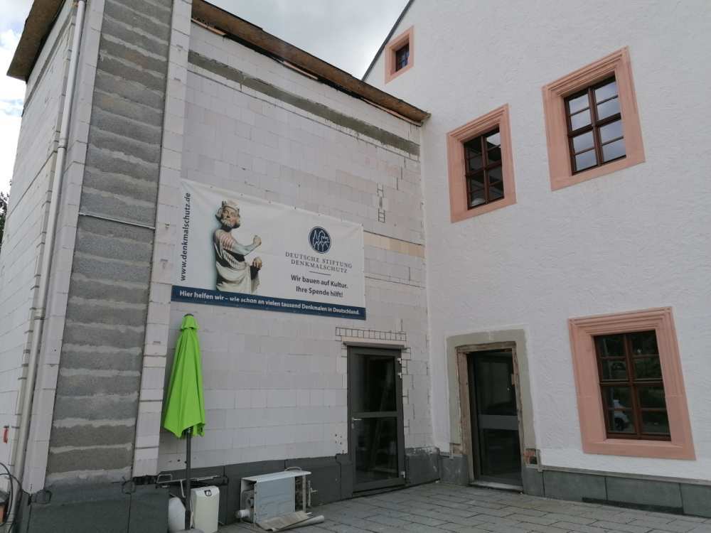 Query successful Außenansicht eines modernen, noch im Bau befindlichen Anbaus an einem historischen Gebäude mit einem Banner der Deutschen Stiftung Denkmalschutz. Der neue Anbau dient als barrierefreie Zuwegung und Fluchtweg. (Link öffnet Bild vergrößert in einem Popupfenster)