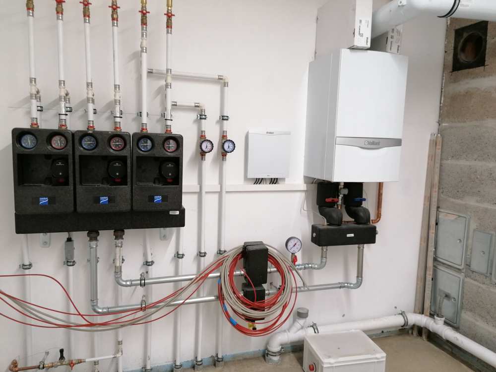Eine moderne Gas-Brennwerttherme mit Pumpengruppen und komplexer Rohrleitungsinstallation an einer Wand. (Link öffnet das Foto vergrößert in einem Popupfenster)