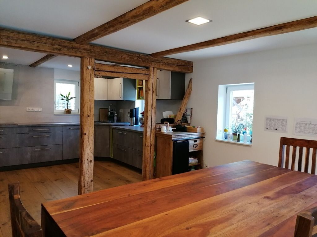 Offener Wohnraum mit moderner Einbauküche, Holzbalken und massivem Esstisch. (Link öffnet Bild vergrößert in einem Popupfenster)