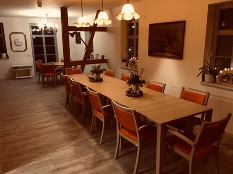 Heller Gemeinschaftsraum mit langer Tafel, orangefarbenen Stühlen und gemütlicher Beleuchtung.